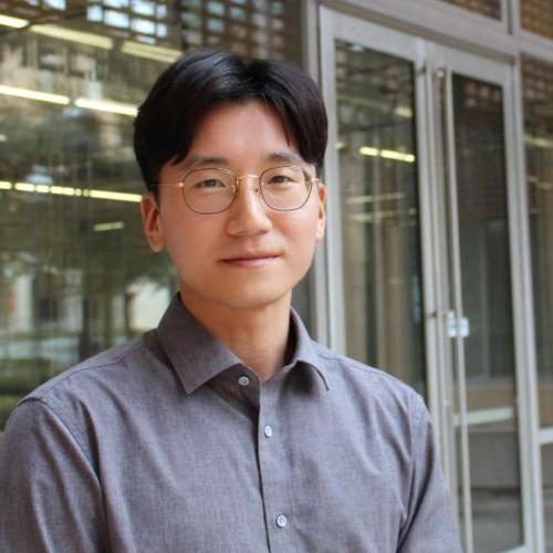 Man with glasses in front of building.
