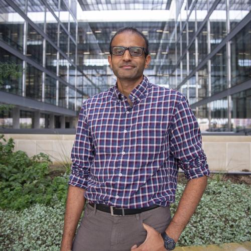 Man with glasses in front of building.