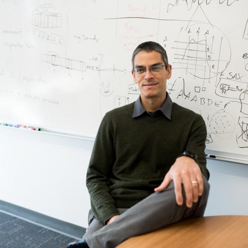 Man with glasses sitting in front of a marker board.