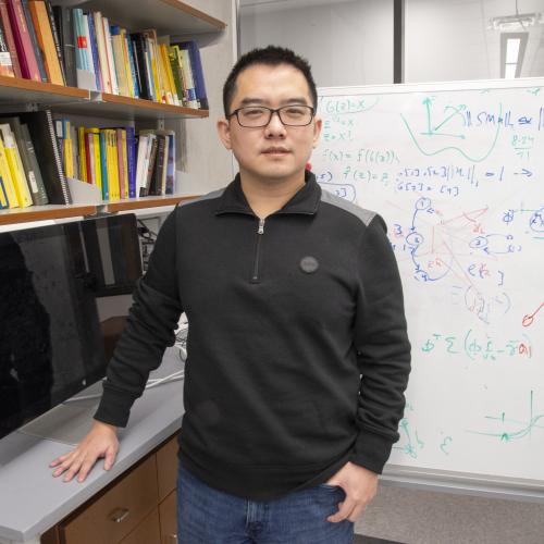 Man with glasses in front of marker board.